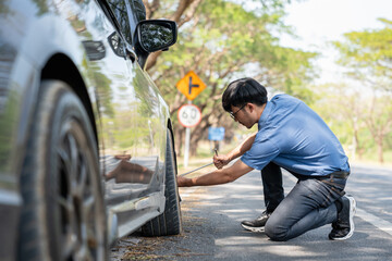 Mechanic or driver providing roadside assistance by changing a flat tire and performing minor...