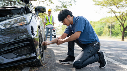 Mechanic or driver providing roadside assistance by changing a flat tire and performing minor...