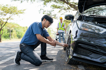 Mechanic or driver providing roadside assistance by changing a flat tire and performing minor...