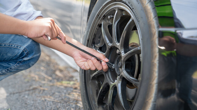 Mechanic or driver providing roadside assistance by changing a flat tire and performing minor repairs on the side of the road during a vehicle breakdown.