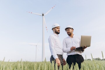 Engineers working in a field of wheat with wind turbines and laptop
