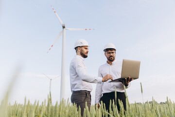 Engineers working on a laptop in a field of wheat with wind turbines