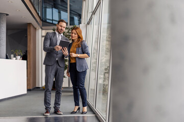 Full length of businesspeople standing at corporation with tablet in hands and looking at it.