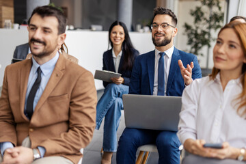 Happy businessman with laptop sitting in audience with laptop and having conversation with...