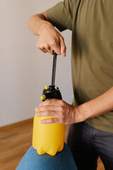 Vertical cropped shot of man pumping yellow water sprayer bottle while holding on blue sofa,...