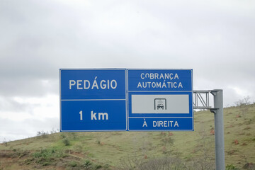 Sinalização rodoviária indicando pedágio a 1 km com opção de cobrança automática à direita. Foto ideal para temas de mobilidade, transporte rodoviário e infraestrutura no Brasil.
