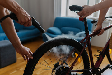 Two friends cyclists cleaning bicycle wheel using high-pressure steam cleaner, removing stubborn...