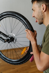 Funny cyclist male jokingly licking tire of mountain bike wheel while holding rag, showcasing...