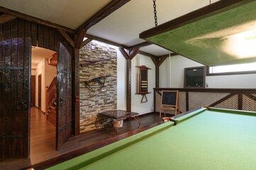 Rustic game room with a pool table, wooden beams, stone wall decor, and antique rifles. An open...