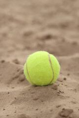 Yellow tennis ball lies on the sand. Sports and recreation concept, summer games. Tennis or paddleball ball. Tennis court near the beach. Paddleball ball on the sand near the water. Outdoor games