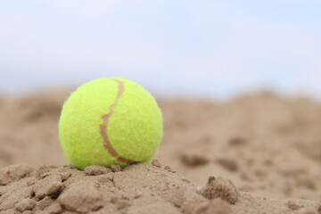 Yellow tennis ball lies on the sand. Sports and recreation concept, summer games. Tennis or paddleball ball. Tennis court near the beach. Paddleball ball on the sand near the water. Outdoor games