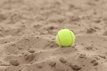 Yellow tennis ball lies on the sand. Sports and recreation concept, summer games. Tennis or paddleball ball. Tennis court near the beach. Paddleball ball on the sand near the water. Outdoor games