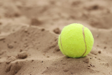 Yellow tennis ball lies on the sand. Sports and recreation concept, summer games. Tennis or paddleball ball. Tennis court near the beach. Paddleball ball on the sand near the water. Outdoor games