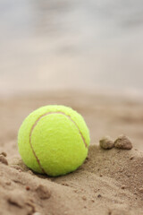Yellow tennis ball lies on the sand. Sports and recreation concept, summer games. Tennis or paddleball ball. Tennis court near the beach. Paddleball ball on the sand near the water. Outdoor games