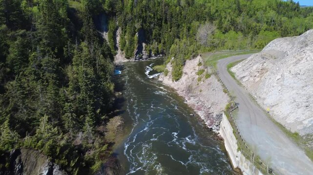 Aerial view of a winding salmon river flowing between rocky cliffs in a lush forest, featuring a dirt path along the bank of the Mitis River in Price, Quebec, Canada.