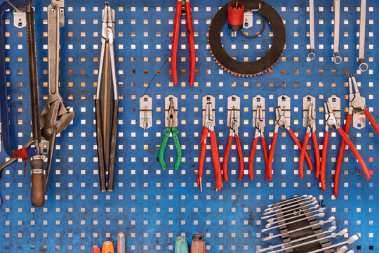 Wall-mounted tool set on pegboard in workshop. Old hand tools is displayed on perforated metal pegboard in a workshop setting. Use for themes related to maintenance and craftsmanship.