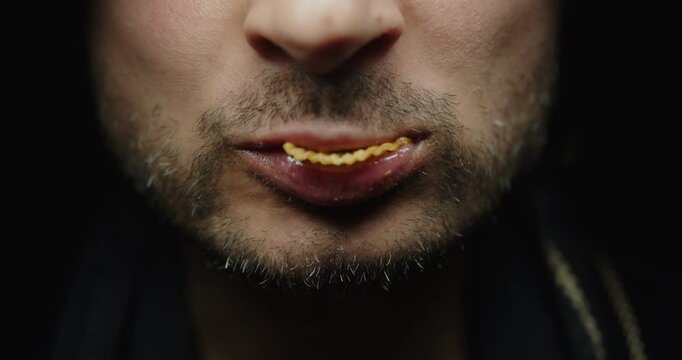 Unshaven sloppy Man eats chips. Close-up on lower part of face. On dark background