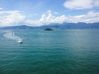 A small boat moving in the distance on the ocean with a mountain background on a sunny day
