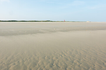 Vast, wide, empty beach, a red lighthouse in the far distance