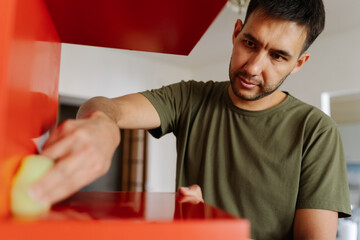Portrait of focused janitor using cleaning cloth, wiping dusty dirty red shelf showcasing...