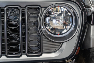 LED headlights of a modern and expensive black car, hood and radiator grille. Front LED headlight on a black SUV car. Glossy black premium car LED headlights close-up. Modern SUV car headlight. 