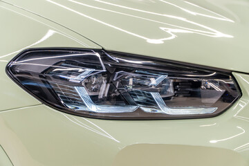 LED headlights of a modern and expensive green car, hood and radiator grille. Front LED headlight on a orange SUV car. Gloss green premium car LED headlights close-up. Modern sport SUV car headlight. 