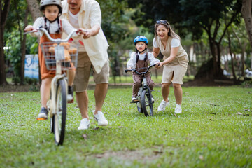 A family of three riding bikes in a park. A man is riding a bike with a child on it