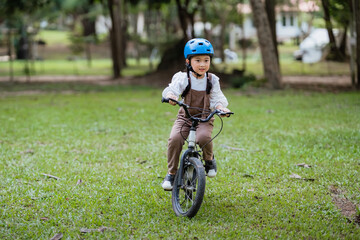 Fototapeta premium A young child is riding a bicycle in a park. The child is wearing a helmet and a backpack