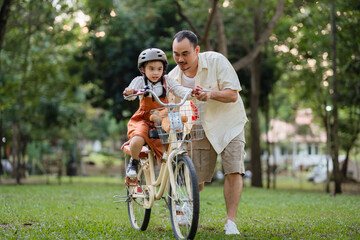 A man is helping a child ride a bike. The child is wearing a helmet. The bike has a basket