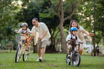 A family of four riding bikes in a park. A man is running to catch up with his children