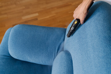 Professional cleaning service worker using steam cleaner to remove dirt and stains from blue sofa...