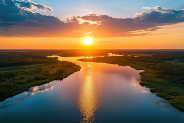 Fototapeta premium Scenic sunset over a river. Aerial view of a tranquil river winding through a lush landscape at golden hour. Reflecting sunlight paints the water. Dramatic clouds complete the serene scene