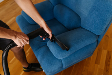 Top view of cleaning service worker washing blue upholstered sofa with vacuum cleaner, providing...