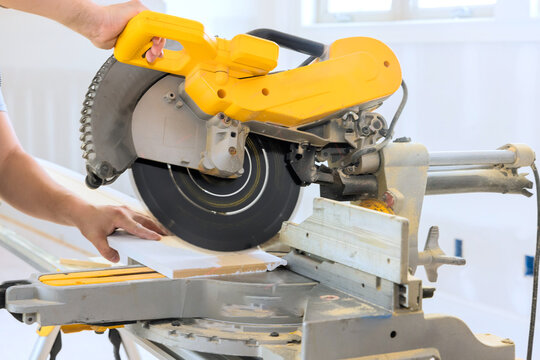 Craftsman operates miter saw to cut wooden materials for project in well lit workshop setting.