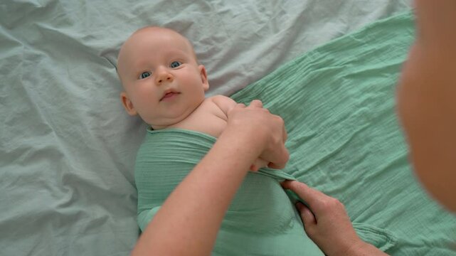 Mother gently swaddling her newborn baby on a bed, creating a peaceful and intimate moment of bonding, love, and care during early stages of motherhood. Slowmotion video.