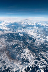 Beautiful aerial view of a large mountain range landscape in winter covered with snow under a cloudy sky. High resolution.