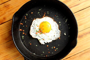There is a cast iron frying pan with a fried egg on a wooden table.