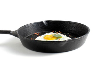 On a white background there is a cast iron frying pan with a fried egg.