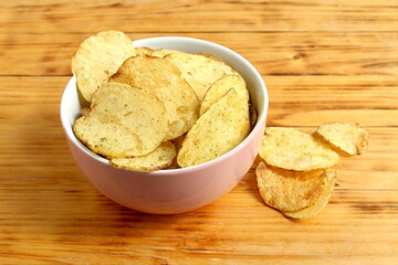There is a bowl full of potato chips on the wooden table.