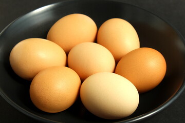 On a black background, there are chicken eggs in a black plate.
