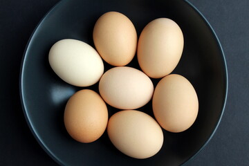 On a black background, there are chicken eggs in a black plate.