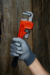 Adjustable pipe wrench in hand worker on wooden background.
