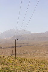 High-voltage power lines cut through Yazd’s arid landscape, framed by distant mountains and barren terrain under a clear desert sky.