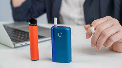 A woman demonstrates different types of cigarettes. An e-cigarette, a disposable vape, and a...