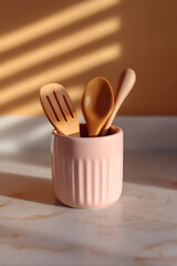 Wooden cooking utensils in a pink holder sit on a bright marble surface.