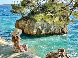A girl in a stylish hat stands on the Croatian coast in Brela, admiring the stunning views of the...
