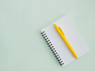 notepad, paper clips and a yellow pen on a light green background 