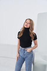 Young woman in a black turtleneck and blue jeans poses confidently with one hand in pocket,...