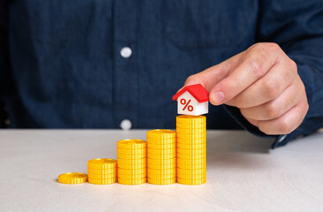A man places a house on top of a staircase made of coins. Saving for a house. Down payment and...