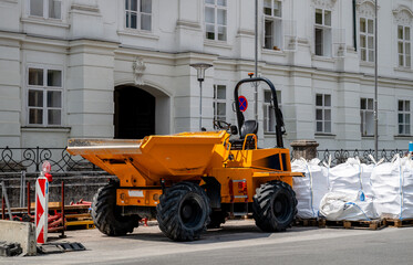 Bright yellow construction dumper truck parked near white building with industrial materials